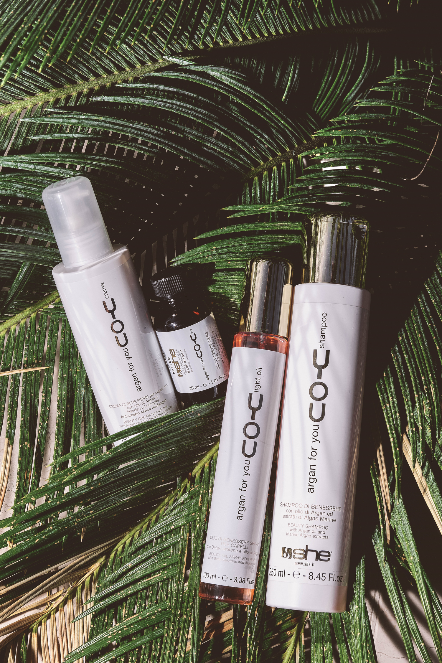 Four she professional hair products laying on plants